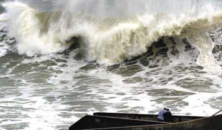big, big wave overshadowing two people on a pier